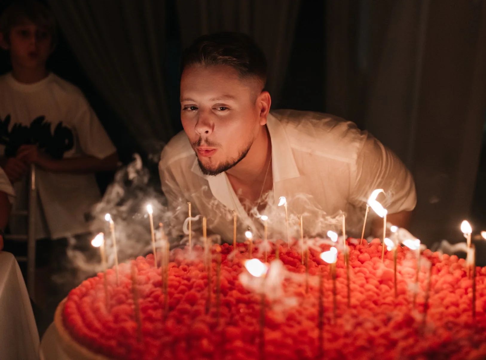 A guest blowing out candles on a dramatic raspberry celebration cake