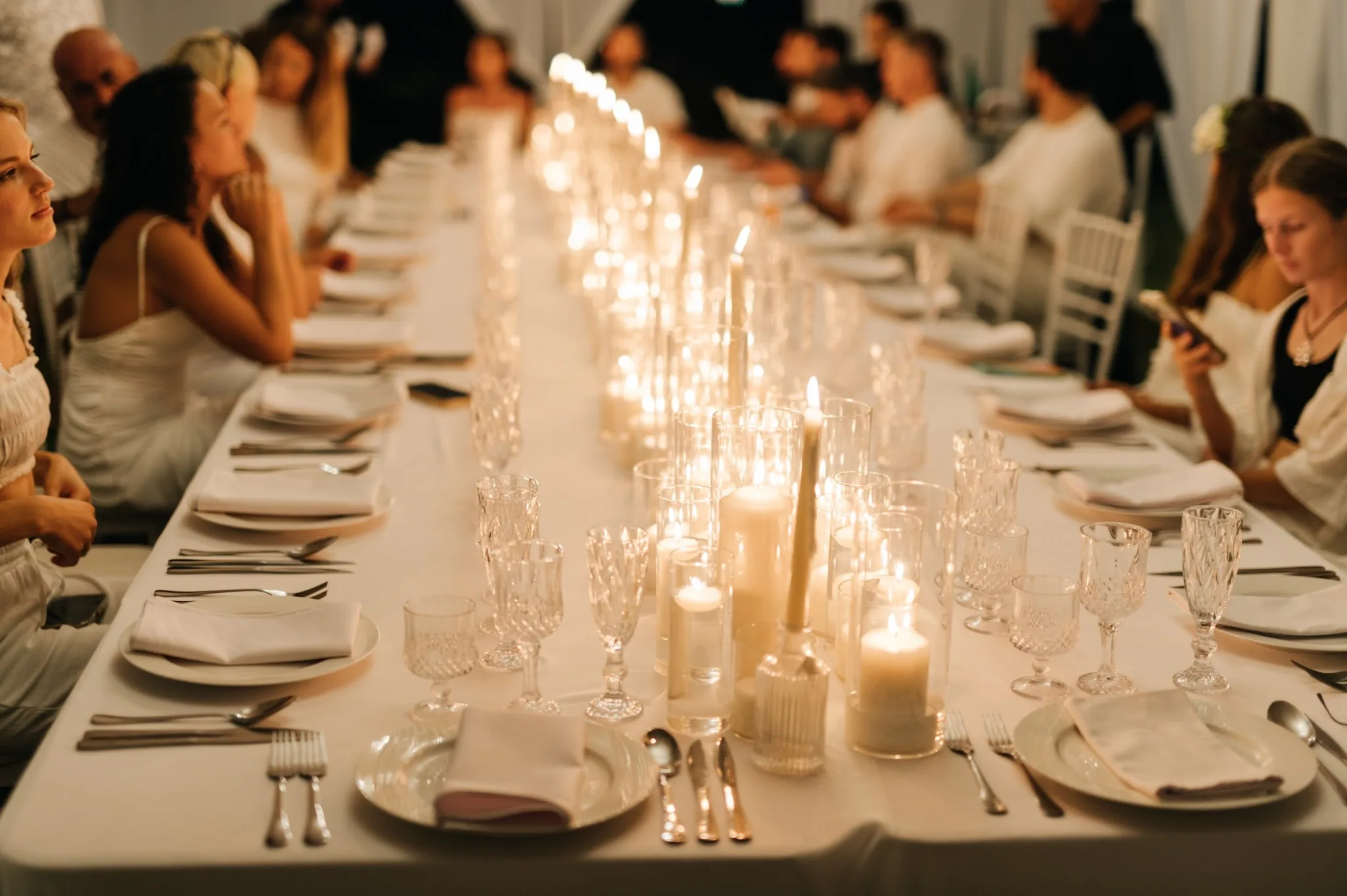 A long candlelit dinner table with guests gathered on both sides